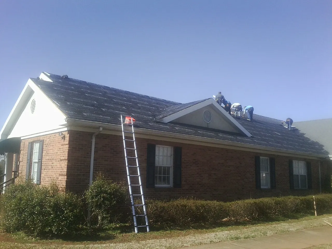 Crew tearing shingles off a brick ranch roof with a ladder set — Metal Roof Repair work by our crew in Walters