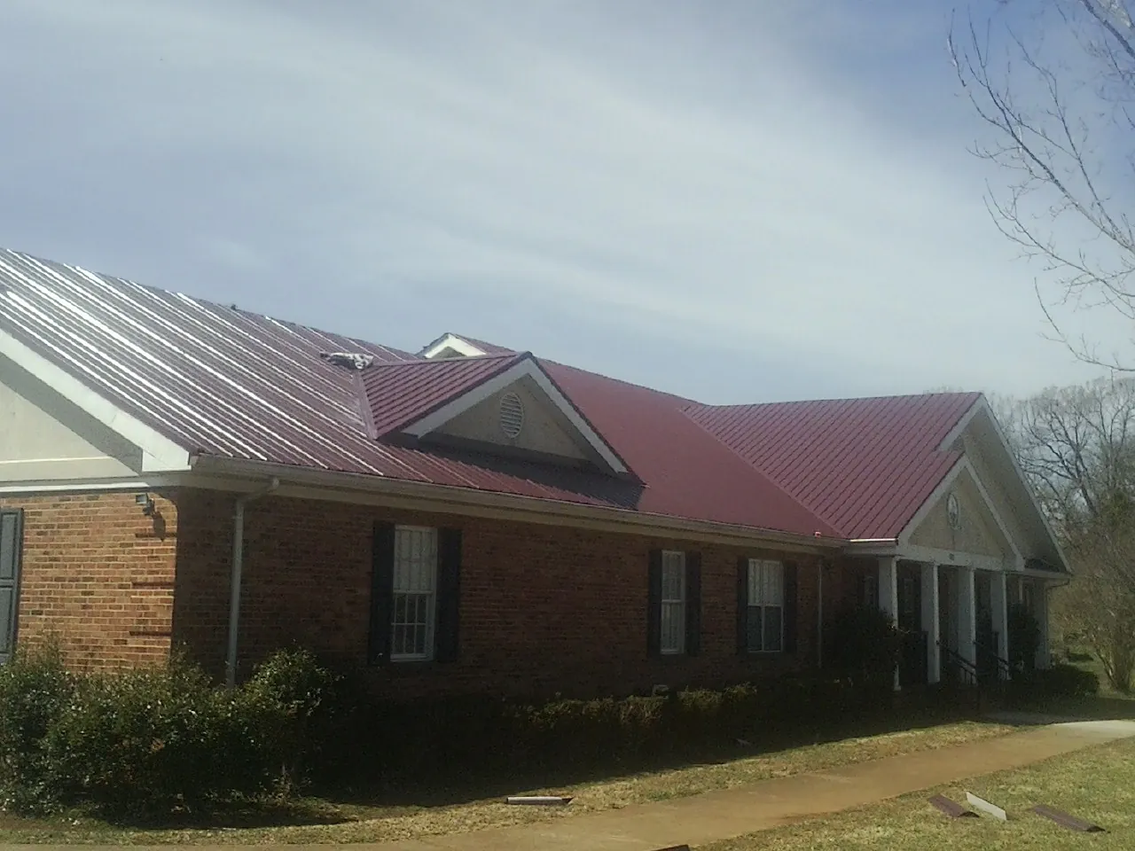 Red metal roof with gabled entries on a long brick building, from a Hail Damage Roof Repair job in Walters