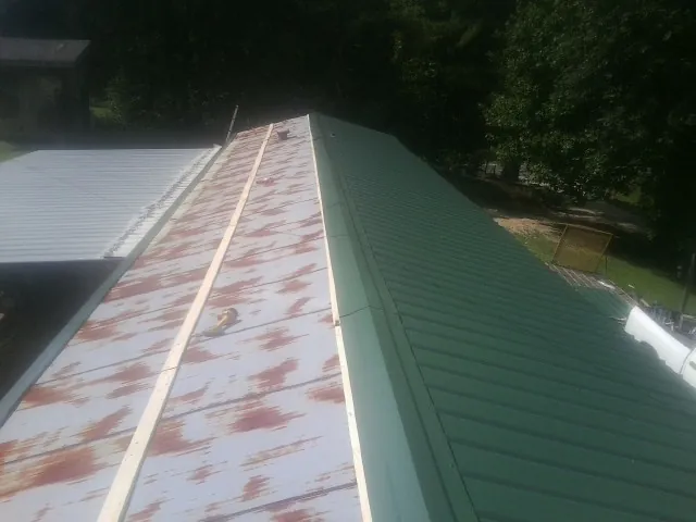 Old rusted panels beside newly installed green metal roofing — Wind Damage Roof Repair by Roofing Brothers in Walters
