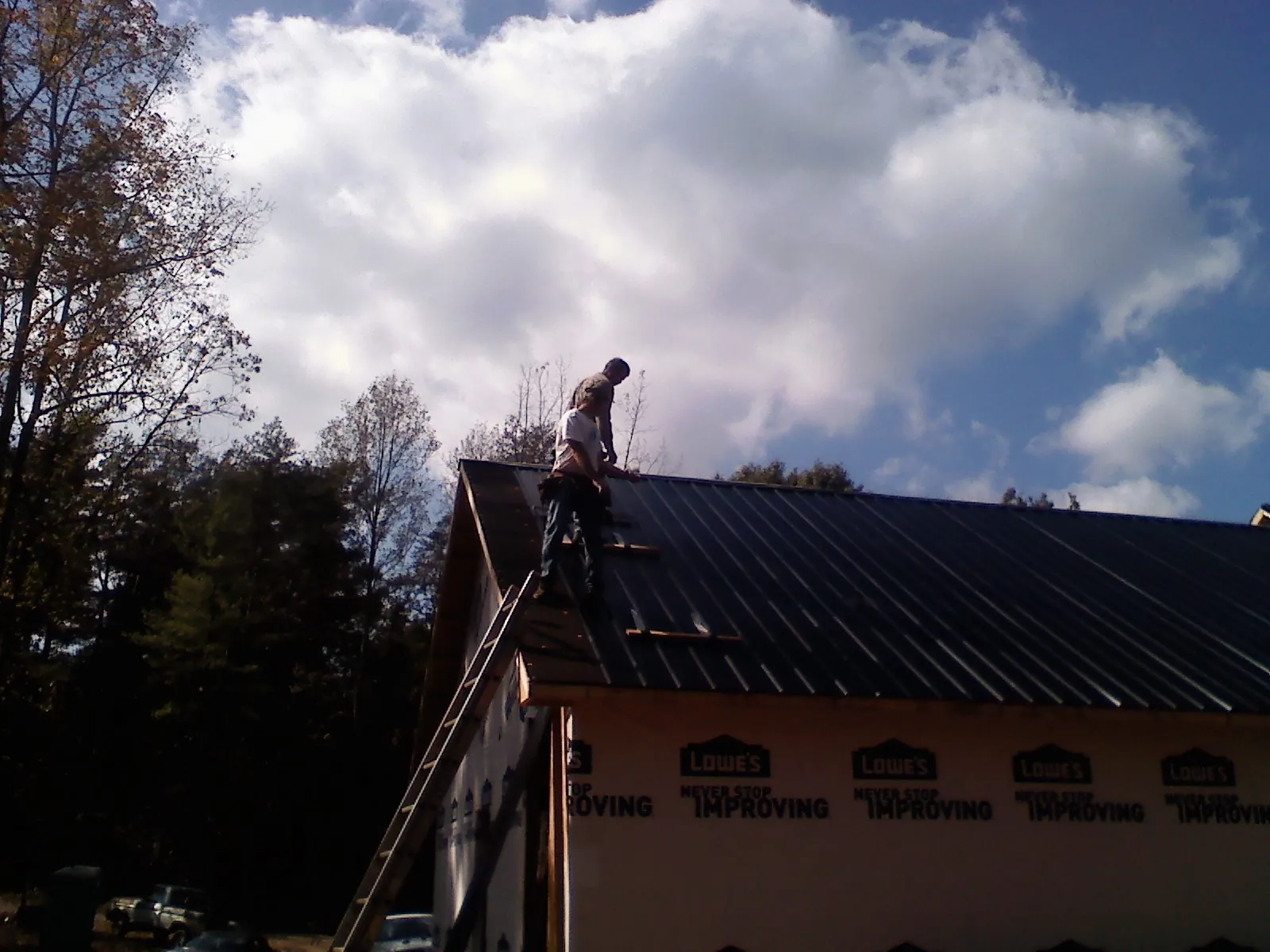 Roofer fastening dark metal panels high against a cloudy sky, from a Roof Inspection job in Walters