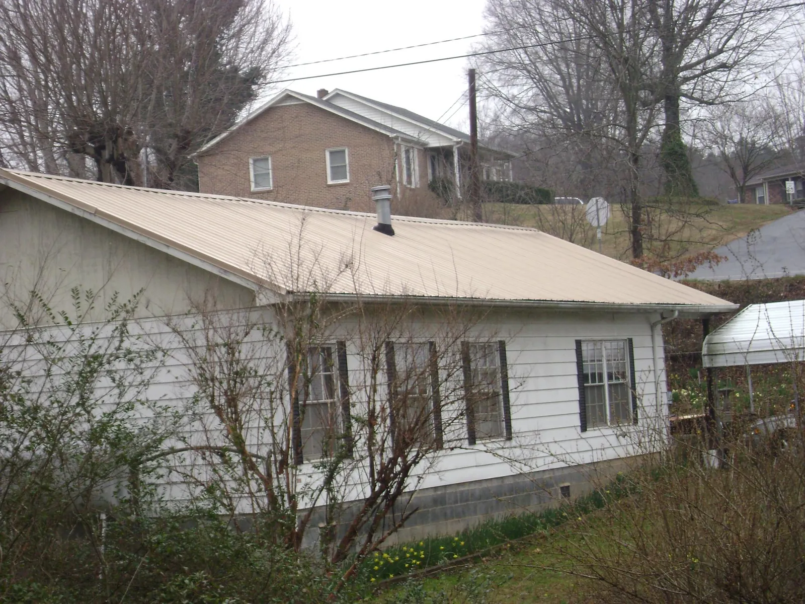 Tan metal roof on a white sided house set into a hillside — Commercial Roofing by Roofing Brothers in Walters
